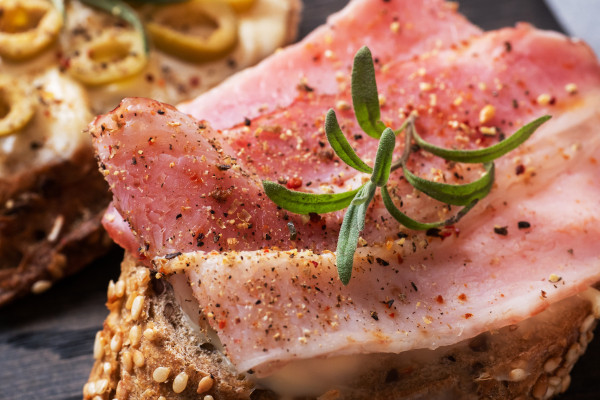2400-wholegrain-bread-sandwiches-with-cream-cheese-bacon-and-olives-on-a-wooden-cutting-board-a-glass-of-white-wine-gray-concrete-background