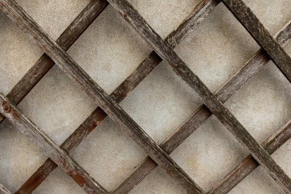 2400-a-close-up-view-of-a-weathered-wooden-trellis-showcasing-its-intricate-diamond-pattern-against-a-textured-background