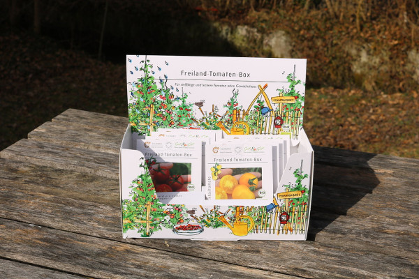 Produktbild der Culinaris BIO Freiland-Tomaten-Box mit Aufdruck einer Gartenillustration und mehreren Samentütchen auf einem Holztisch im Freien.